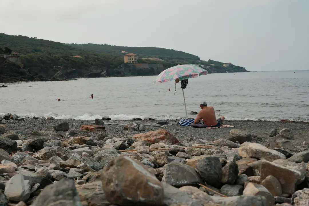 A rocky Mediterranean cove, pine-covered headland beyond