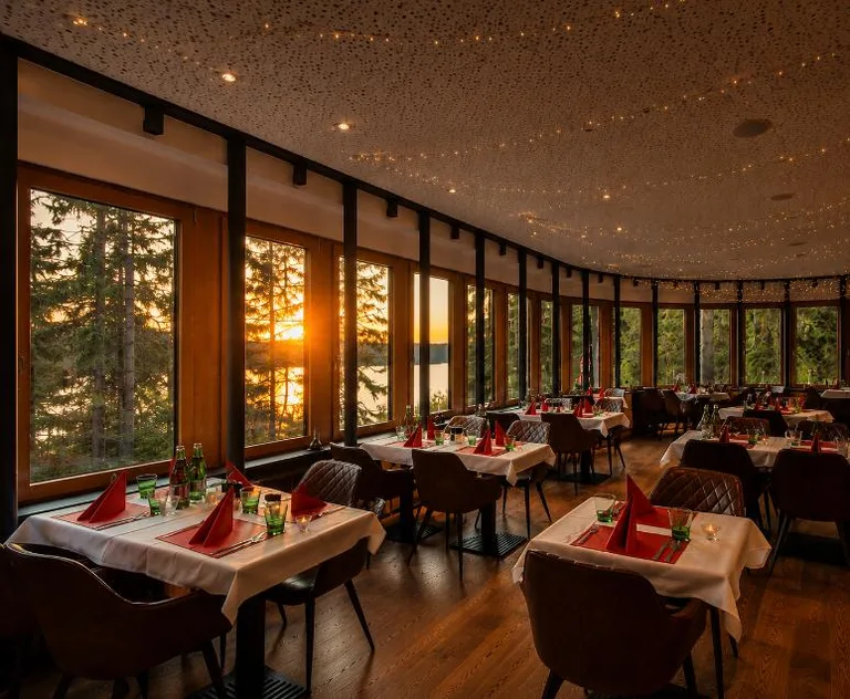 The Montanie Resort dining room at sunset, floor-to-ceiling windows over the forest and lake